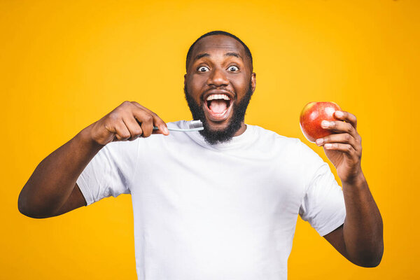 Man with tooth brush. Image of young shirtless African man holding a toothbrush with toothpaste and apple, smiling while standing against yellow background.