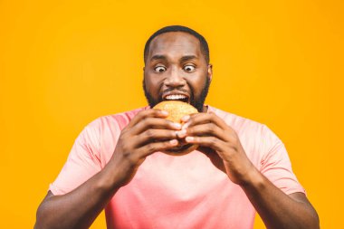 Sarı arka planda izole edilmiş hamburger yiyen Afrikalı genç bir Amerikalı..