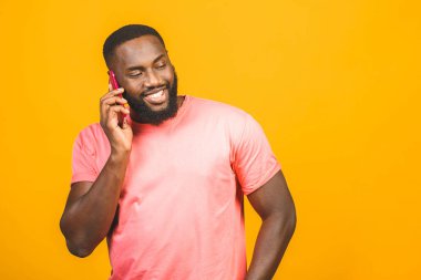 Telefondaki adam. Neşeli siyah adam cep telefonuyla konuşuyor ve sarı arka planda tek başına dururken gülümsüyor.. 
