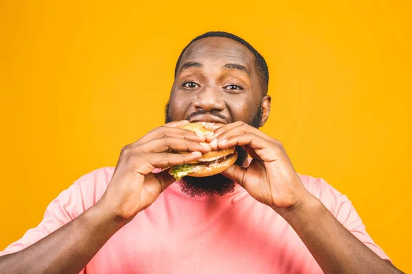 Sarı Arka Planda Izole Edilmiş Hamburger Yiyen Afrikalı Genç Bir — Stok fotoğraf