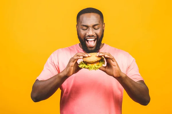 Sarı Arka Planda Izole Edilmiş Hamburger Yiyen Afrikalı Genç Bir — Stok fotoğraf