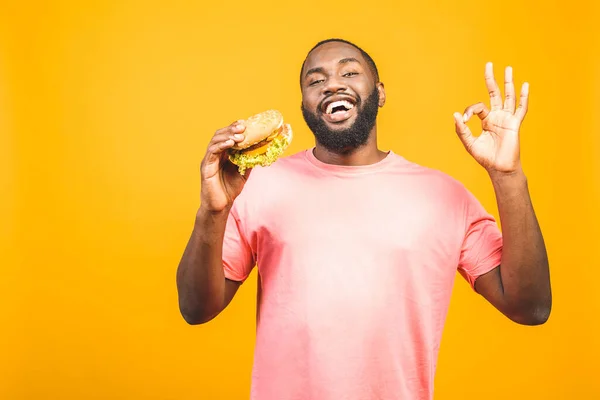 Sarı Arka Planda Izole Edilmiş Hamburger Yiyen Afrikalı Genç Bir — Stok fotoğraf