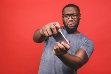 Kırmızı arka planda izole edilmiş bir şekilde cep telefonuyla oyun oynayan neşeli, siyah Afrikalı Amerikalı bir adamın portresi..