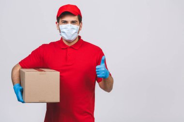 Kırmızı şapkalı, boş tişörtlü, maske eldivenli teslimatçı eleman beyaz arka planda boş karton kutu tutuyor. Servis karantina salgını Coronavirus virüsü 2019-ncov konsepti.