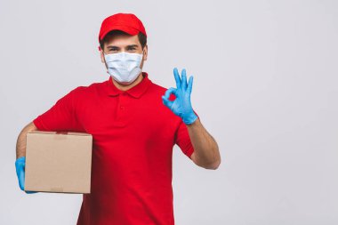 Kırmızı şapkalı, boş tişörtlü, maske eldivenli teslimatçı eleman beyaz arka planda boş karton kutu tutuyor. Servis karantina salgını Coronavirus virüsü 2019-ncov konsepti.