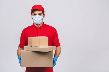 Kırmızı şapkalı, boş tişörtlü, maske eldivenli teslimatçı eleman beyaz arka planda boş karton kutu tutuyor. Servis karantina salgını Coronavirus virüsü 2019-ncov konsepti.