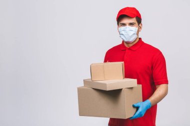 Kırmızı şapkalı, boş tişörtlü, maske eldivenli teslimatçı eleman beyaz arka planda boş karton kutu tutuyor. Servis karantina salgını Coronavirus virüsü 2019-ncov konsepti.