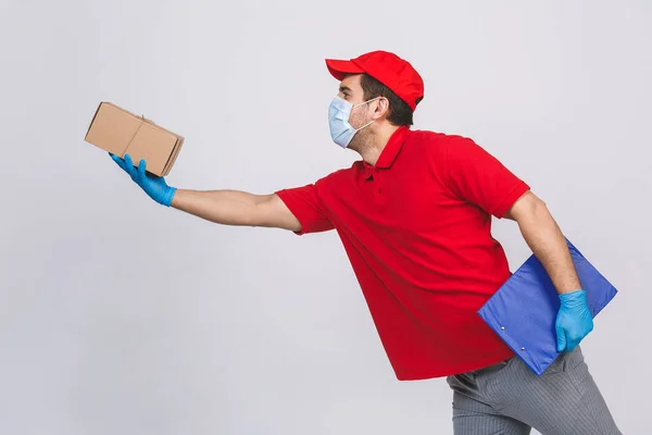 Delivery man employee in red cap blank t-shirt uniform face mask gloves hold empty cardboard box isolated on white background. Service quarantine pandemic coronavirus virus 2019-ncov concept.