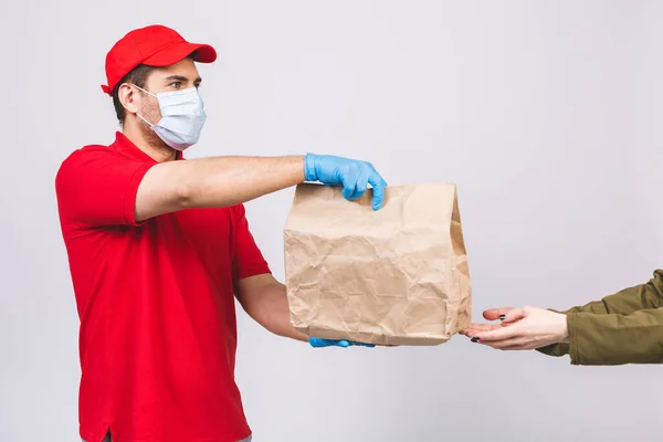 Delivery man employee in red cap blank t-shirt uniform face mask gloves hold empty cardboard box isolated on white background. Service quarantine pandemic coronavirus virus 2019-ncov concept.