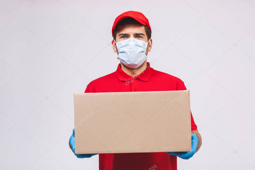 Delivery man employee in red cap blank t-shirt uniform face mask gloves hold empty cardboard box isolated on white background. Service quarantine pandemic coronavirus virus 2019-ncov concept.