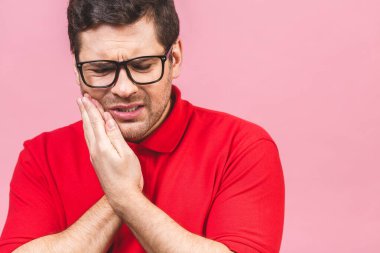 Diş ağrısı konsepti. Kapalı alanda genç bir erkek acı çekiyor, yanağını eliyle tutuyor, kötü diş ağrısından muzdarip, acı dolu bir ifade..