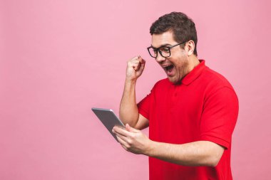 Mutlu galip. Pembe arka planda duran mutlu sakallı genç bir adam görüntüsü. Tablet bilgisayarı kullanılıyor.