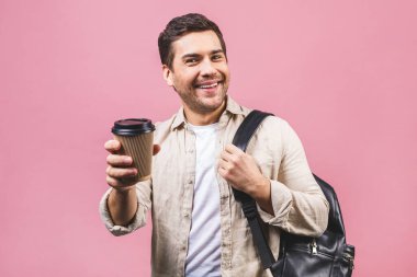 Sırt çantalı yakışıklı bir adam pembe arka planda kahve fincanı tutuyor. Gülümseyen öğrenci portresi. Yolculuğa çıkan neşeli adamların stüdyo fotoğrafları..