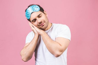 Mavi uyku maskeli huzurlu, uykulu genç bir adamın portresi. Pembe arka planda izole edilmiş.