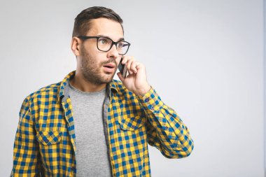 Kareli gömlekli mutlu genç adam gri arka planda cep telefonuyla konuşuyor.