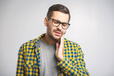 Diş ağrısı. Hayal kırıklığına uğramış genç adam yanağına dokunuyor ve evdeki kanepede otururken gözlerini kapalı tutuyor.