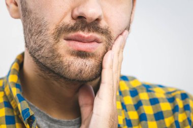 Diş ağrısı. Diş ağrısından muzdarip yakışıklı genç adam, yakın plan, beyaz arka planda ağrıyı durdurmak için yanağına dokunuyor. Güçlü diş ağrısı