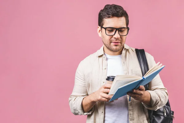 Handsome young man with backpack and book, isolated on pink background. Portrait of student reading book. Adult male student with school bag carrying text books.