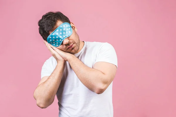 Portrait of nice calm peaceful sleepy young man with blue sleeping mask. Isolated over pink background.
