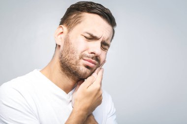 Diş ağrısı. Diş ağrısından muzdarip yakışıklı genç adam, yakın plan, beyaz arka planda ağrıyı durdurmak için yanağına dokunuyor. Güçlü diş ağrısı