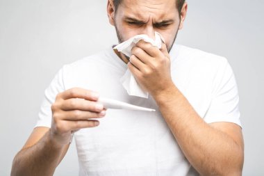 Adam üşütmüş, grip olmuş, burnu akıyor. Sağlık ve tıbbi konsept beyazda izole edildi. Sıcaklık kontrol ediliyor. 