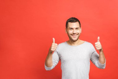 Başparmak başarı için! Kendinden emin, genç ve yakışıklı bir adam kırmızı arka planda dikilirken başparmağını kaldırıyor ve gülümsüyor..
