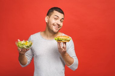 Salata ve hamburger, sağlıklı ve abur cubur arasında seçim yapmayı düşünen bir adam. Diyet konsepti. Sağlıklı yemek ile kötü yemek arasında seçim yapmak. Organik gıdalar fast food 'a karşı, beyazlar üzerinde izole.. 