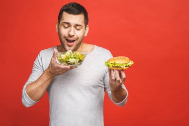 Salata ve hamburger, sağlıklı ve abur cubur arasında seçim yapmayı düşünen bir adam. Diyet konsepti. Sağlıklı yemek ile kötü yemek arasında seçim yapmak. Organik gıdalar fast food 'a karşı, beyazlar üzerinde izole.. 