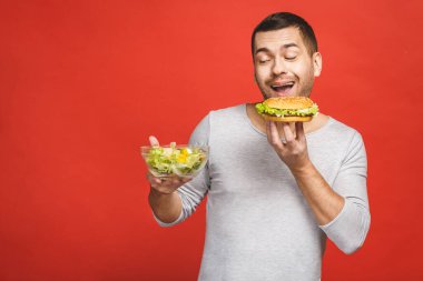 Salata ve hamburger, sağlıklı ve abur cubur arasında seçim yapmayı düşünen bir adam. Diyet konsepti. Sağlıklı yemek ile kötü yemek arasında seçim yapmak. Organik gıdalar fast food 'a karşı, beyazlar üzerinde izole.. 