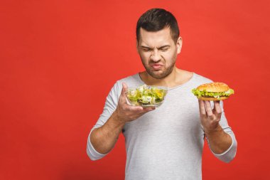 Salata ve hamburger, sağlıklı ve abur cubur arasında seçim yapmayı düşünen bir adam. Diyet konsepti. Sağlıklı yemek ile kötü yemek arasında seçim yapmak. Organik gıdalar fast food 'a karşı, beyazlar üzerinde izole.. 