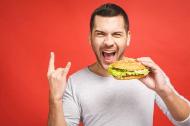 Hamburger tutan genç bir adam. Öğrenci fast food yiyor. Burger yararlı bir yemek değildir. Çok aç bir adam. Diyet konsepti. Kırmızı arkaplan üzerinde izole edilmiş.