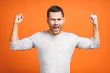 Mutlu galip. Turuncu arka planda dikilirken el kol hareketi yapan ve ağzını açık tutan mutlu genç adam..