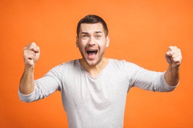 Mutlu galip. Turuncu arka planda dikilirken el kol hareketi yapan ve ağzını açık tutan mutlu genç adam..