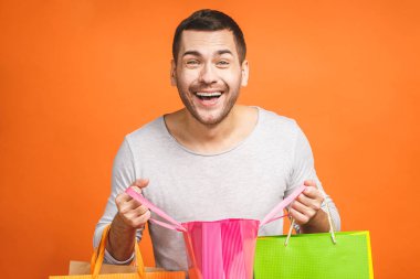 Alışveriş zamanı geldi! Turuncu arka planda renkli kağıt torbaları olan mutlu genç adam..