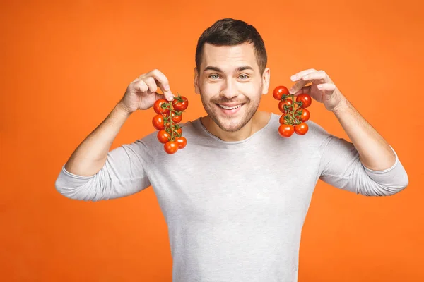 Hombre Joven Con Sostiene Bayas Tomate Aisladas Sobre Fondo Naranja —  Fotos de Stock