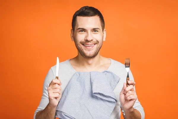 Young happy smiling crazy man holding a fork and a knife. Isolated on orange background.