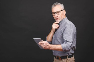 Harika haberlerim var! Yakışıklı, gündelik giyinen ve gözlüklü bir iş adamı dijital tablet kullanıyor ve gülümsüyor, siyah arkaplana karşı izole edilmiş..