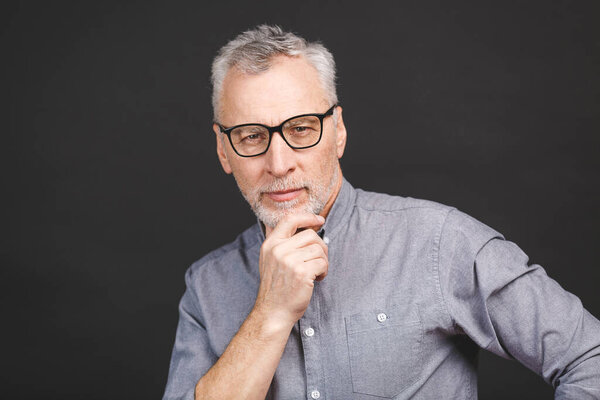 Portrait of a mature businessman wearing glasses isolated against black background. Happy senior man looking at camera with copy space. Close up face of happy successful business man. 