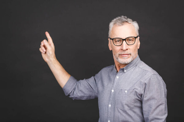 Aged senior man wearing glasses isolated against black background amazed and smiling to the camera while presenting with hand and pointing with finger.