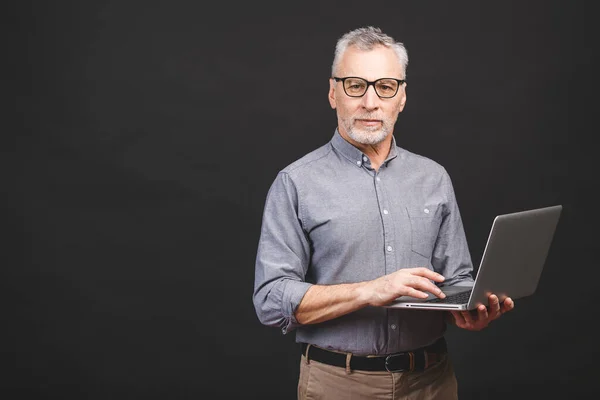 stock image Senior aged bearded old man in eyeglasses holding laptop computer and smiling isolated against black background.