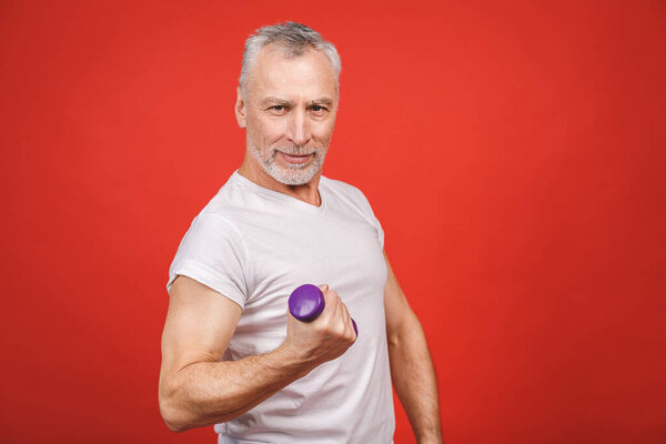 Portrait Of A Senior Man Exercising with dumbbells against red Background.