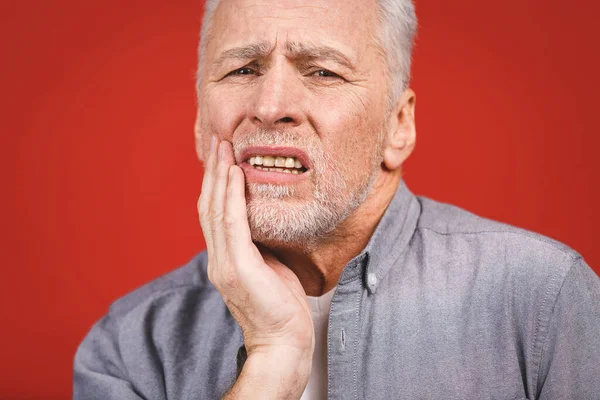 高齢者男苦しみから歯痛に上の赤い背景 — ストック写真