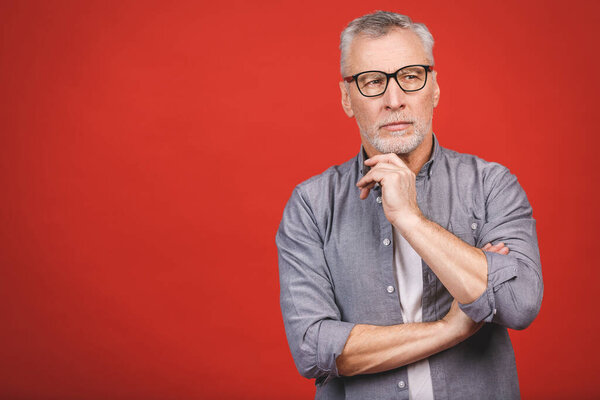 Portrait of a mature serious businessman wearing glasses isolated against red background. Happy senior man looking at camera with copy space. Close up face of happy successful business man. 