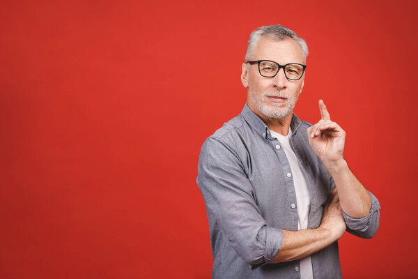 I have a great idea! Portrait of a mature serious businessman wearing glasses isolated against red background. Happy senior man looking at camera with copy space. Close up face of happy successful business man. 