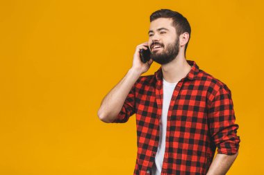 Mutlu gülümseyen genç adam sarı arka planda cep telefonuyla konuşuyor..