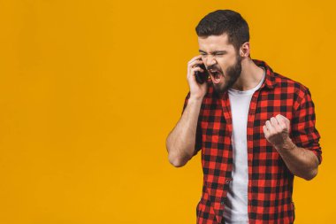 Sinirli genç adam sarı arka planda izole bir şekilde cep telefonundan bağırıyor..  