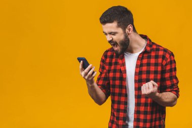 Sinirli genç adam sarı arka planda izole bir şekilde cep telefonundan bağırıyor..  