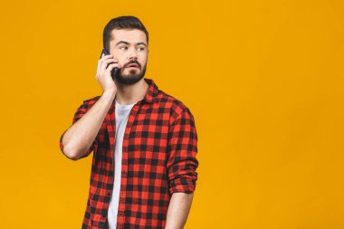 Cep telefonundan konuşan ciddi genç adam sarı arka planda izole edilmiş..