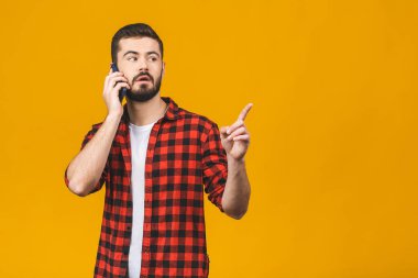 Kırmızı arka planda izole edilmiş bir şekilde işaret ederken sıradan bir şekilde cep telefonu kullanan heyecanlı bir gencin portresi.