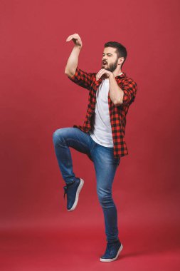 Heyecanlı mutlu bir adamın tam boy portresi parmaklarının ucunda duruyor ve elleri kırmızı arka planda izole bir şekilde uzanıyor..